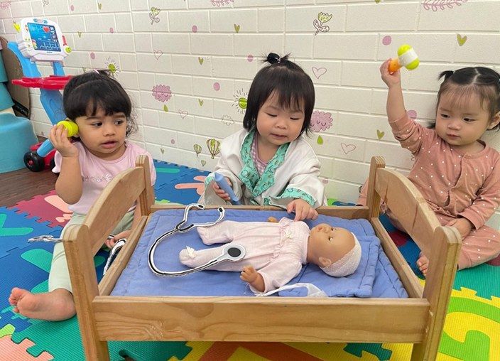 Toddlers engaged in pretend doctor play with a toy baby and stethoscope