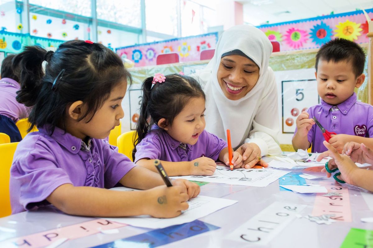 A teacher guiding young children through a hands-on worksheet activity in the playgroup classroom